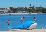 A giant blue floatable plastic whale on a beach with kids playing.